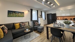Ein modernes Wohnzimmer mit einer Couch, einem Esstisch und einer Küchenzeile inklusive Schränke und Kühlschrank.