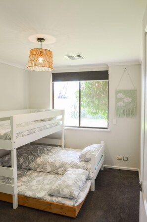 A bedroom with a bunk bed, a window with a view of greenery, a hanging light fixture, and a wall decoration.