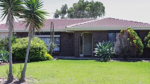 A two-story brick house with a red-tiled roof, a front door with a decorative metal gate, and a well-maintained lawn with various plants.