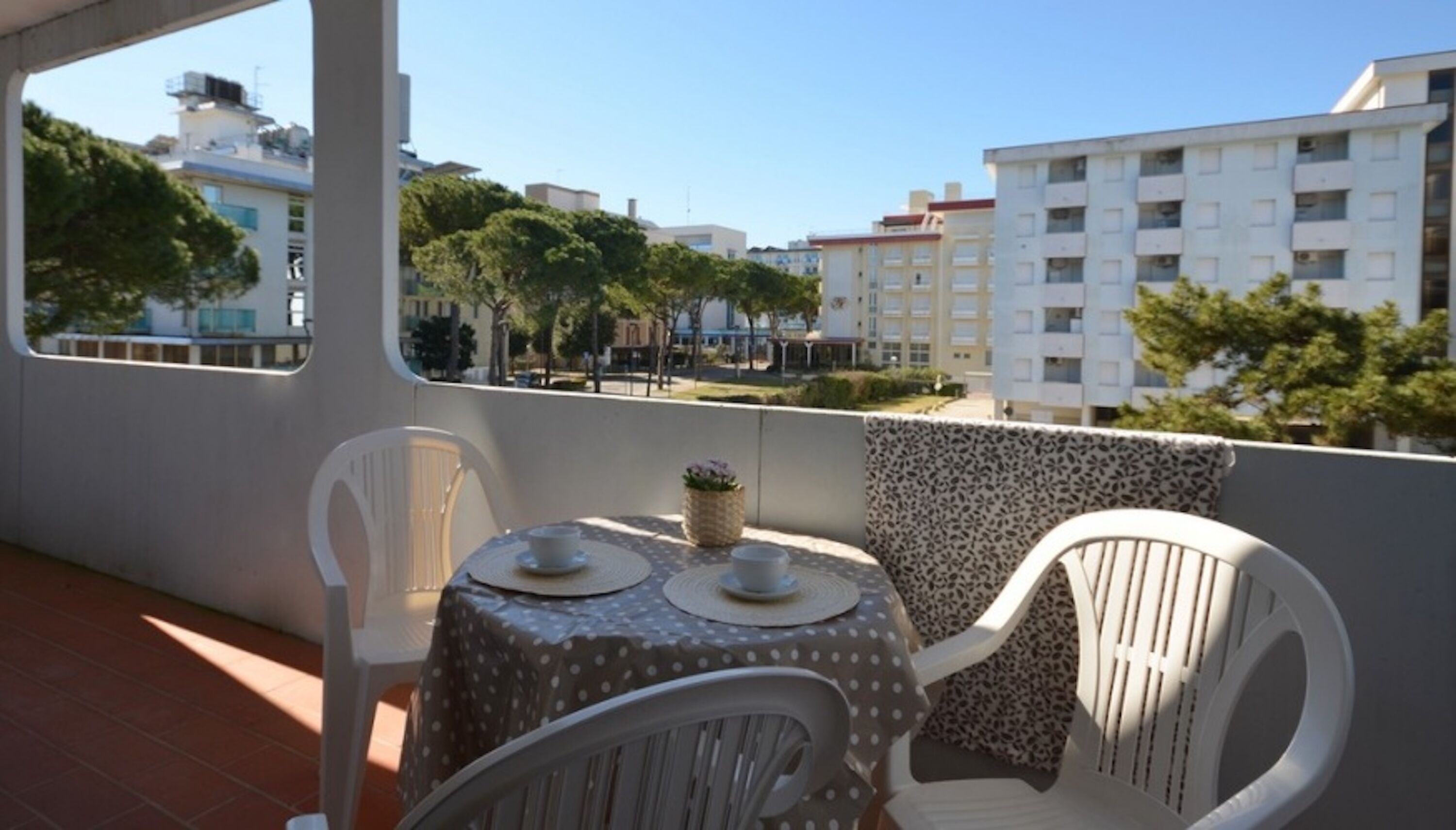 A balcony with a table and chairs, overlooking a cityscape with buildings and trees.