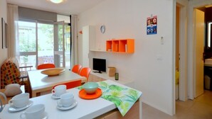 A modern kitchen with white cabinets, a dining area with orange chairs, and a small TV on the wall. - Contemporary renewed house (Bibione)
