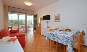 A cozy living area with a red sofa, a dining table with a patterned tablecloth, and a TV on the wall. - Stylish house with a lovely terrace (Bibione)