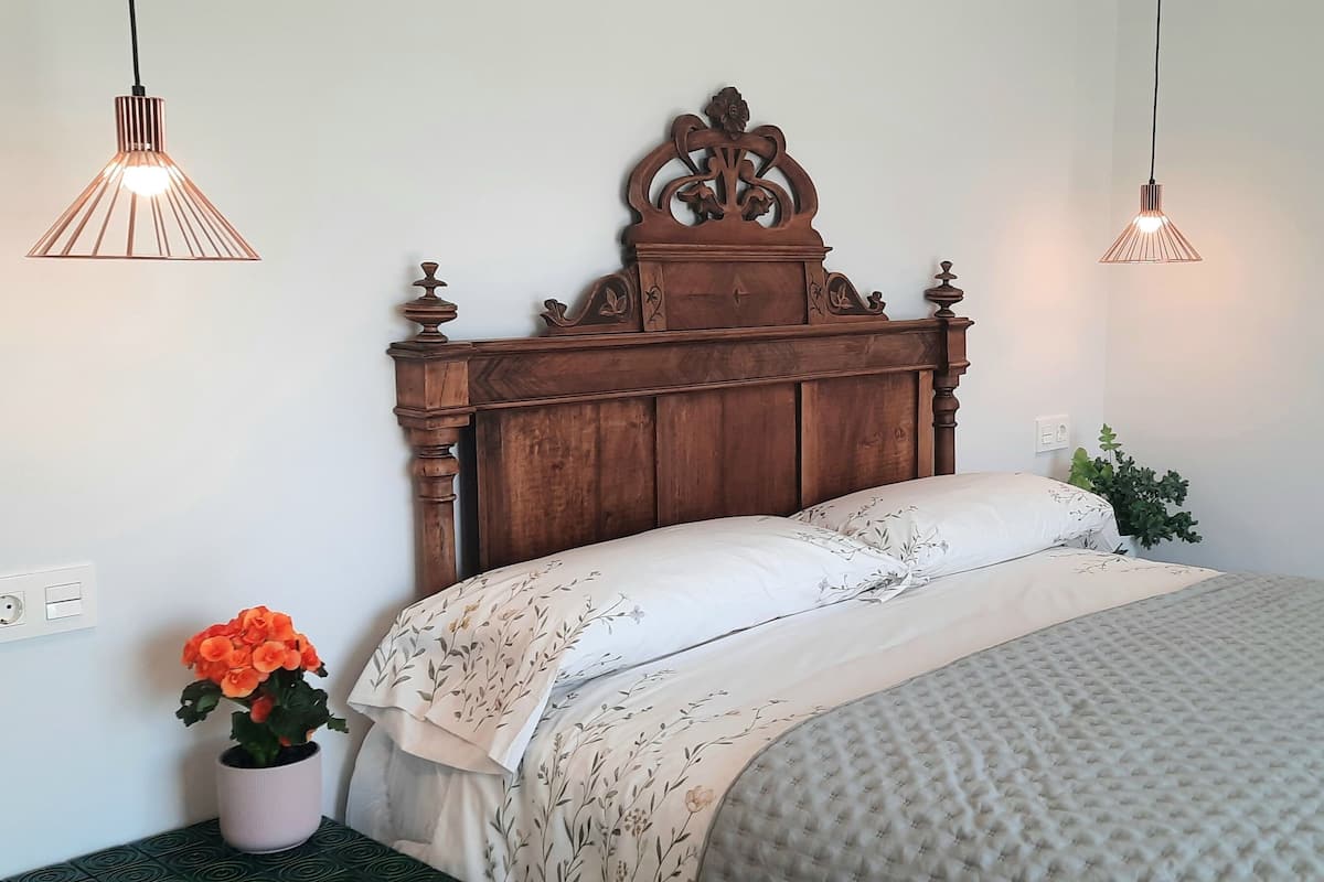 A neatly made bed with a wooden headboard, two bedside lamps, and a potted plant on the nightstand.