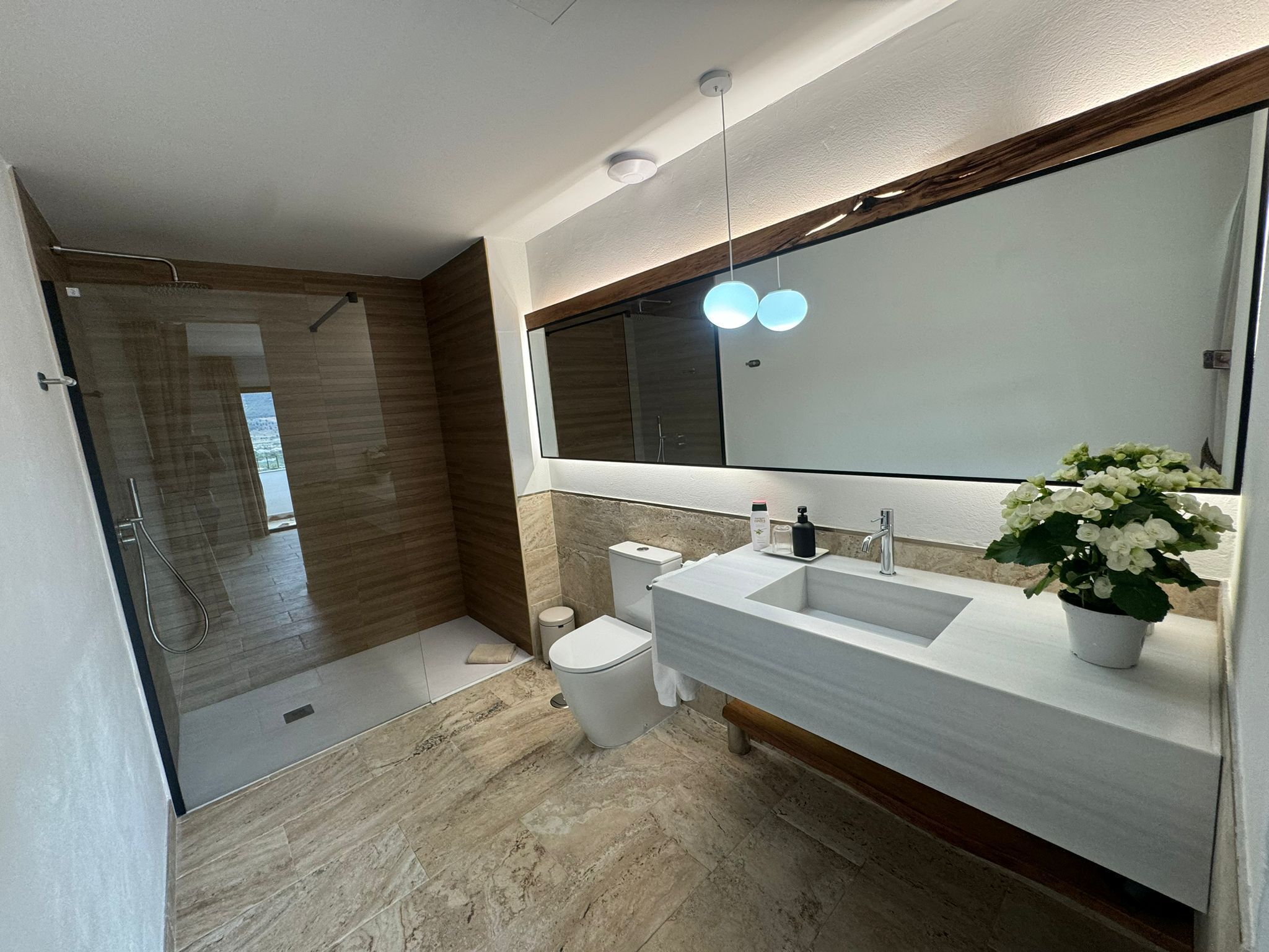 Un baño moderno con ducha a ras de suelo, inodoro y lavamanos con un espejo grande.