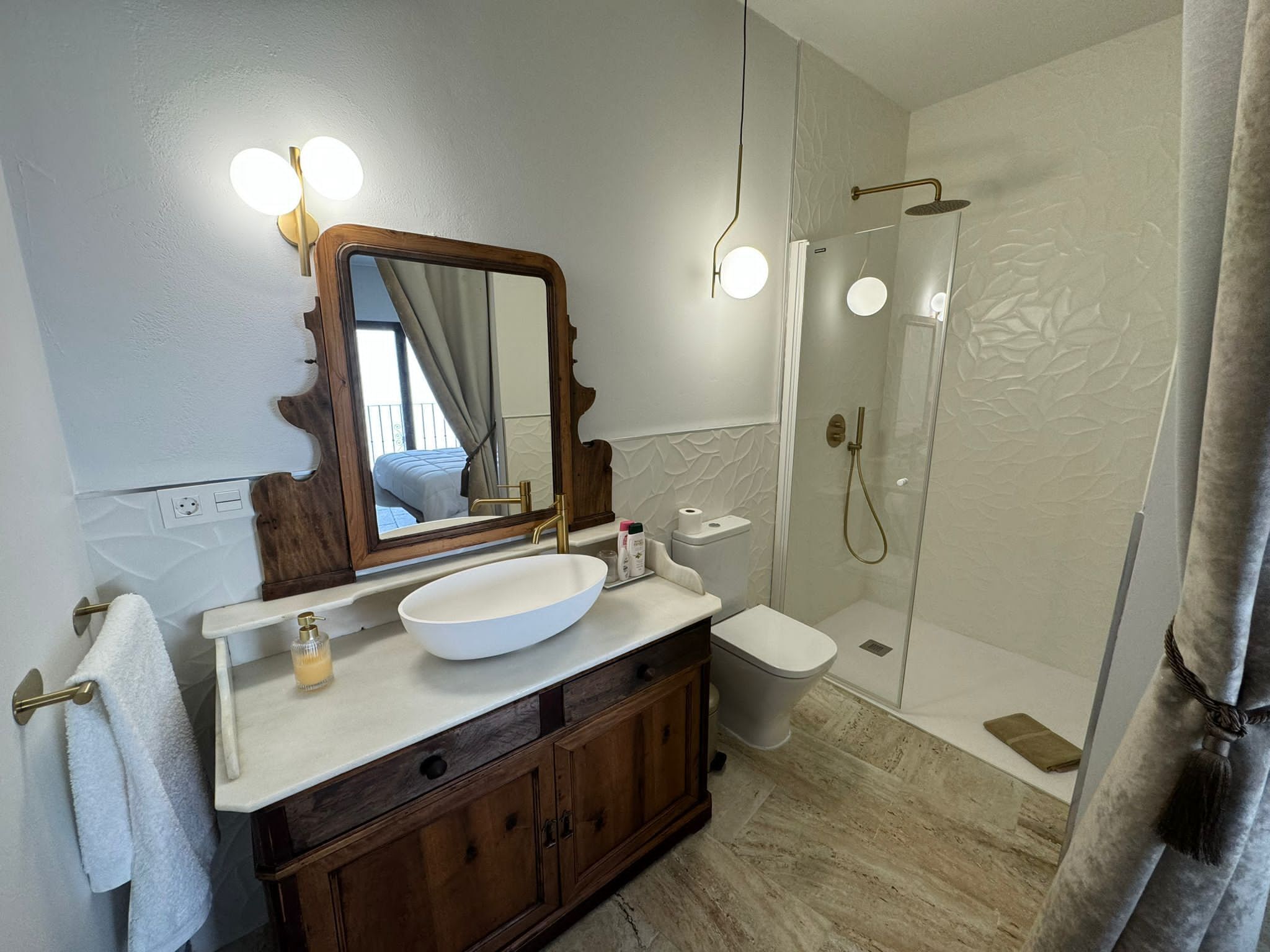 A bathroom with a large mirror, a white sink, a toilet, and a glass-enclosed shower.