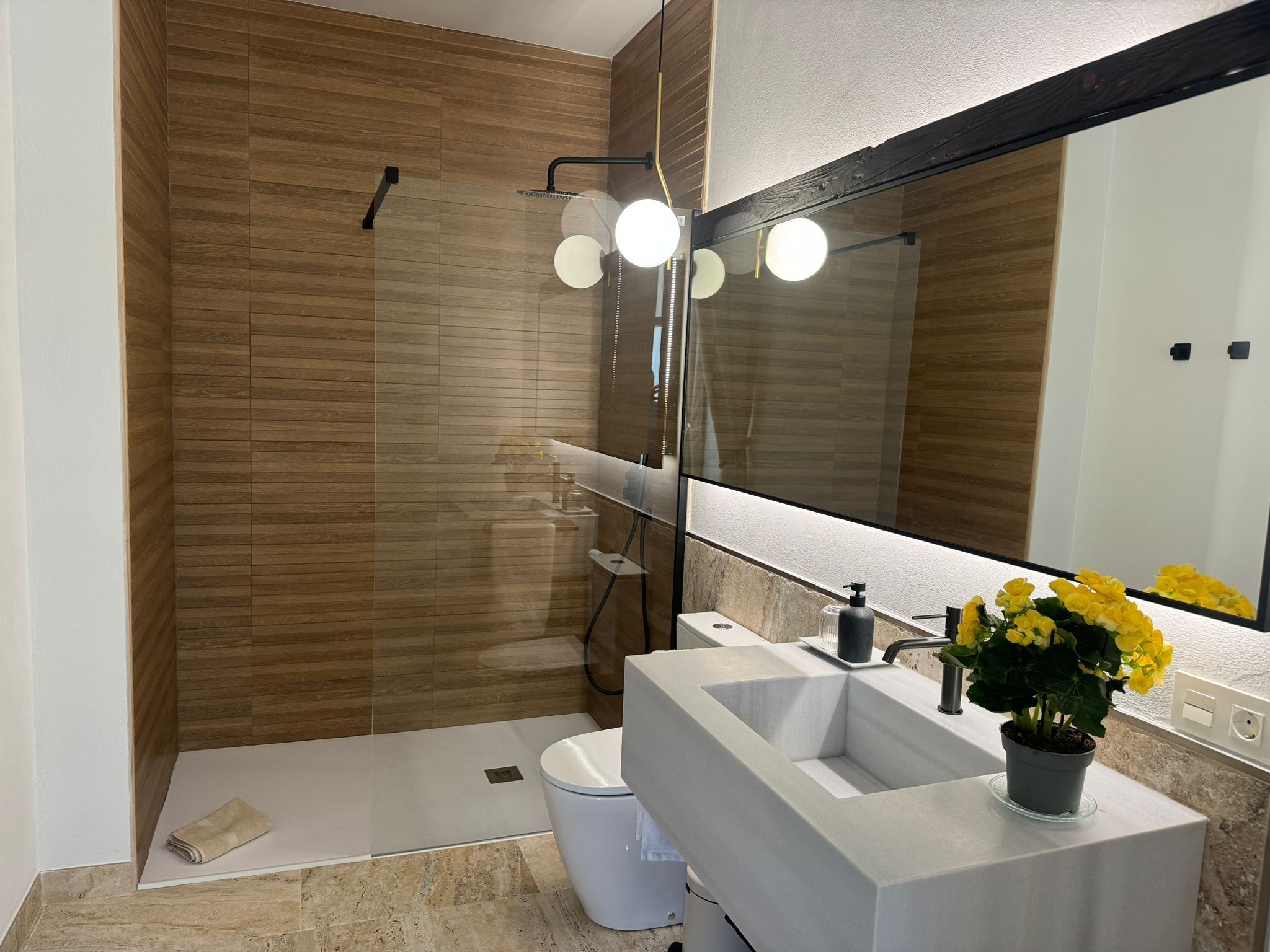 Un baño moderno con un espejo grande, una ducha y un lavabo con una planta en maceta.