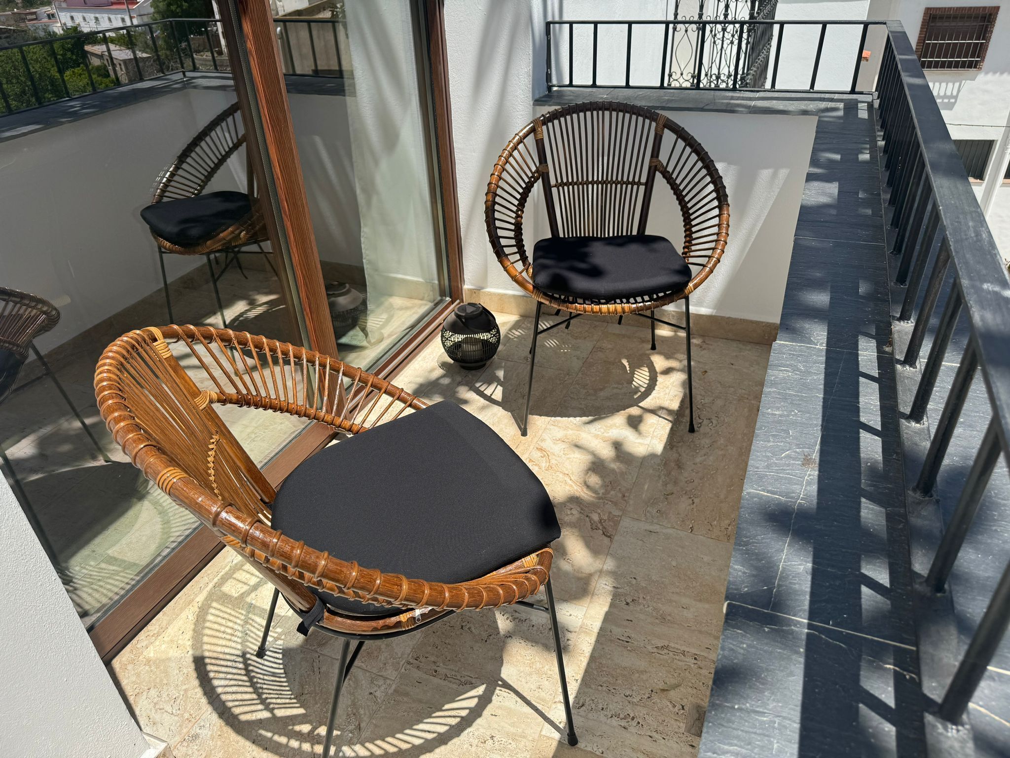 En balkon med to fletstole, et lille bord, en glasdør og gelænder i metal.