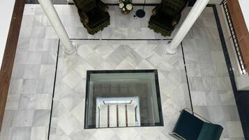 A spacious lobby with a marble floor, a central seating area with two chairs, a small table with flowers, and a staircase.