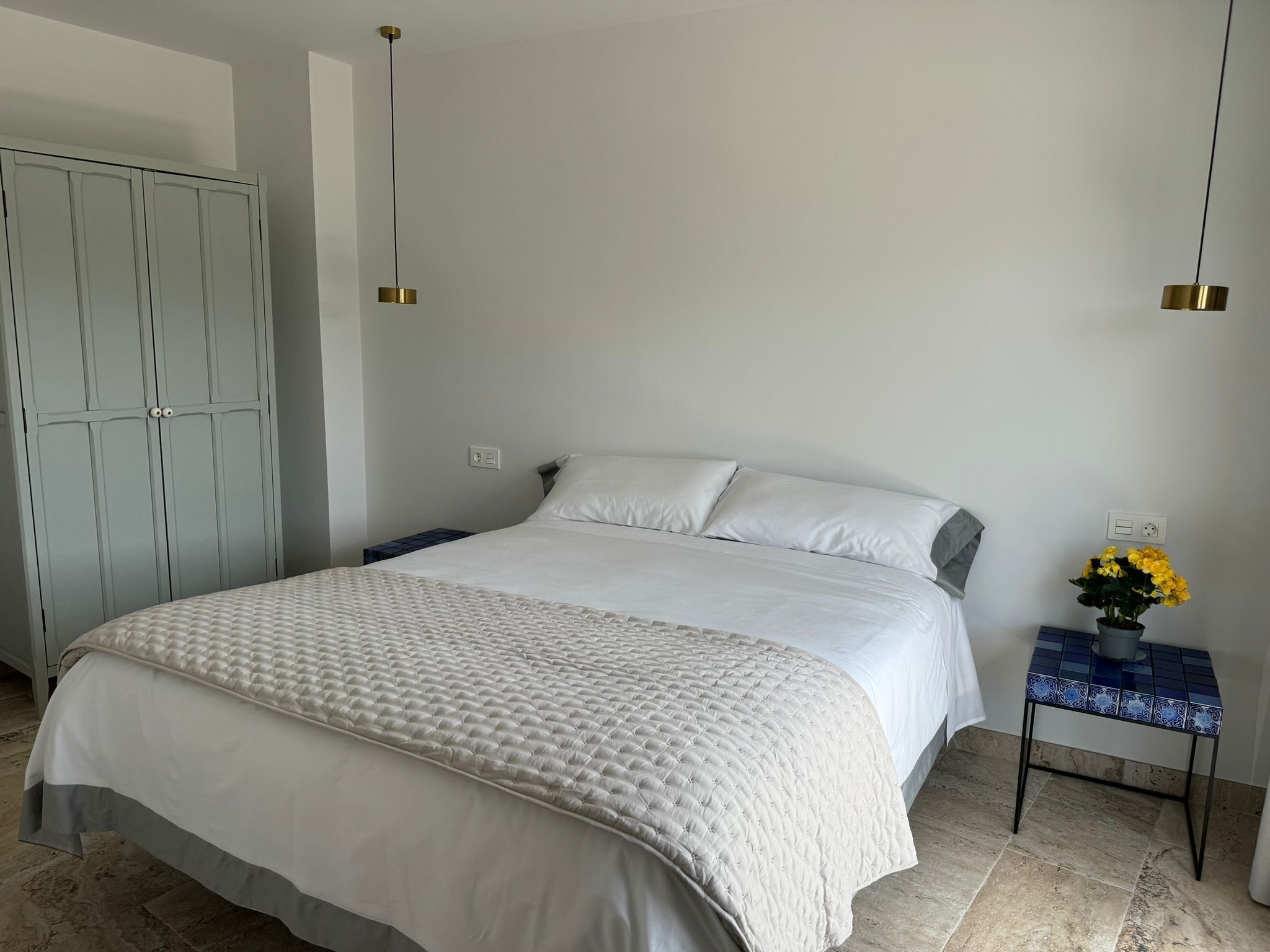 Ein Schlafzimmer mit Bett, Kleiderschrank, Nachttisch, Lampe und Topfpflanze.