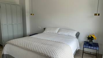 A bedroom with a bed, a wardrobe, a nightstand, a lamp, and a potted plant.