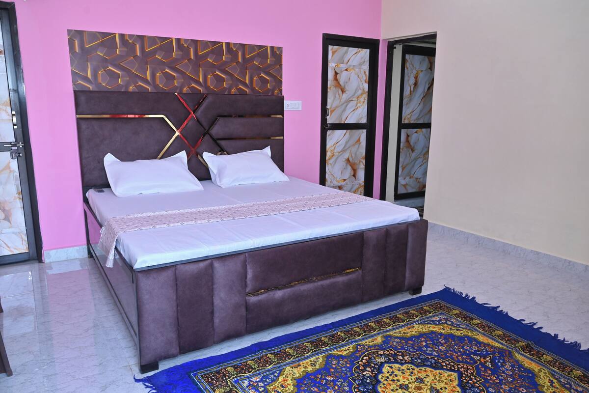 Un dormitorio con una cama grande, cabecera con diseños geométricos, alfombra estampada en azul y una pared de mármol.