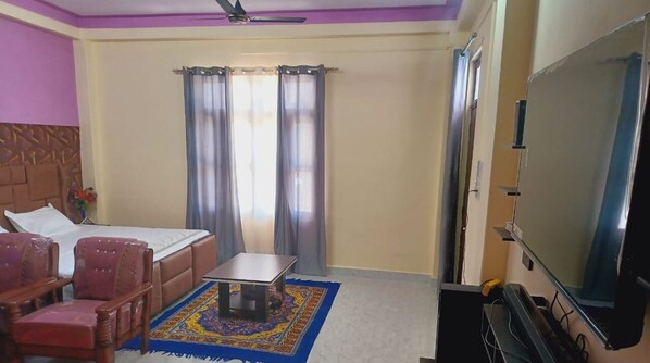 A hotel room with a bed, a desk, a TV, and two chairs. - Sun Shine Haven Retreat Chandi  (Krishangarh)