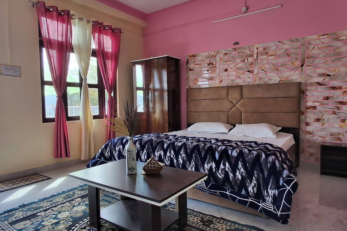 Un dormitorio con cama, una mesa, una ventana con cortinas y vistas al exterior.