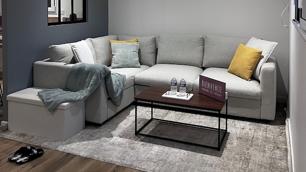 Un salon moderne avec un canapé d’angle gris, une table basse et un tableau encadré accroché au mur.
