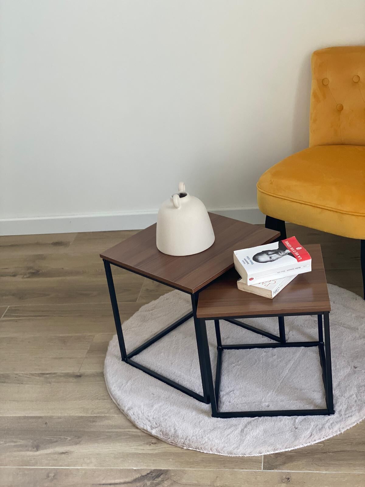 Una pequeña mesa de madera con una tetera blanca y un libro encima, sobre una alfombra redonda.