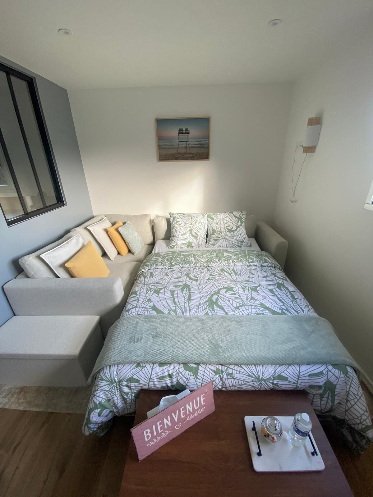 A bedroom with a bed, a sofa, a coffee table, a welcome sign, and a painting on the wall.