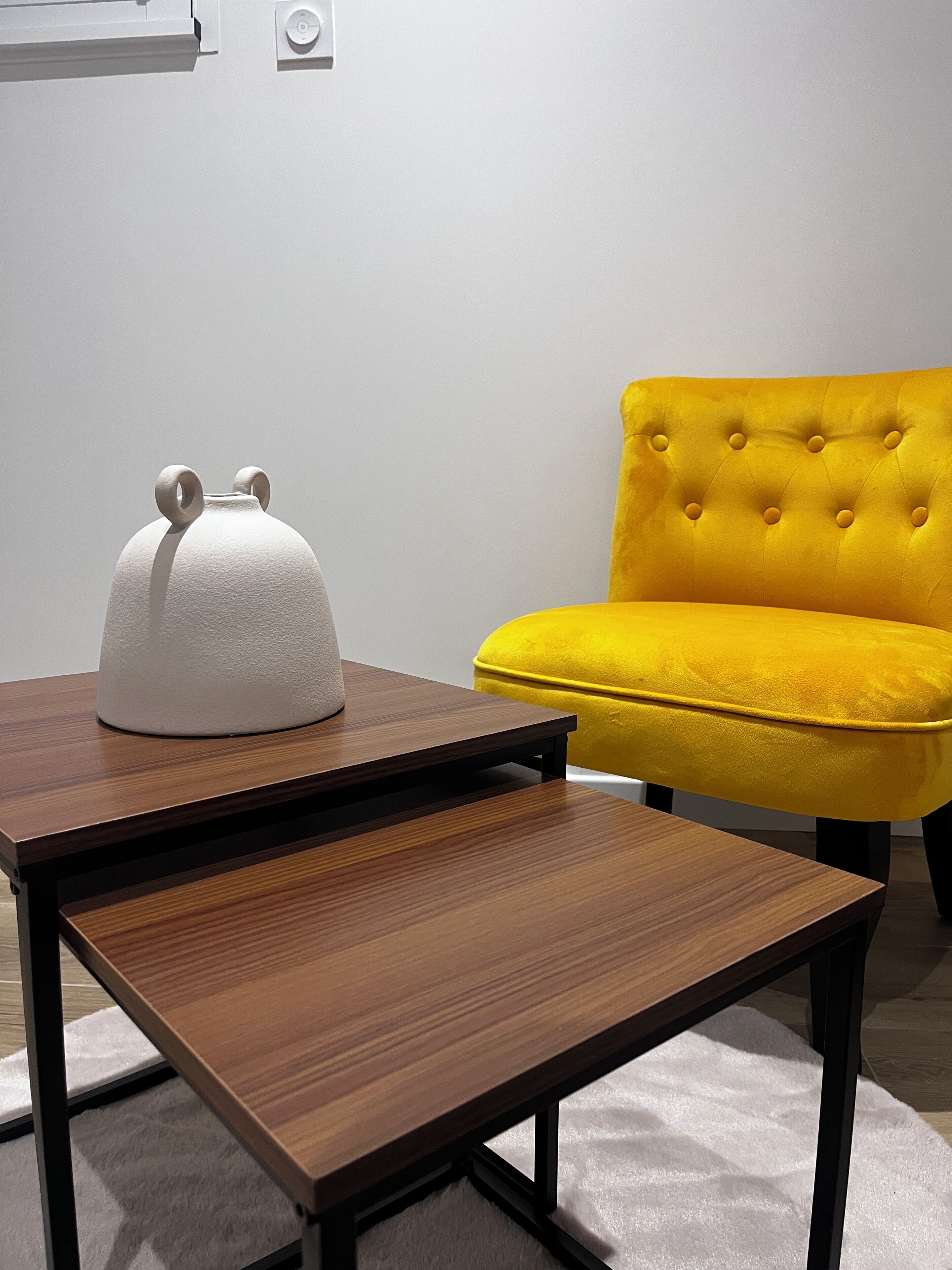 Una habitació moderna amb una taula de fusta, un objecte blanc sobre la taula i una cadira groga.