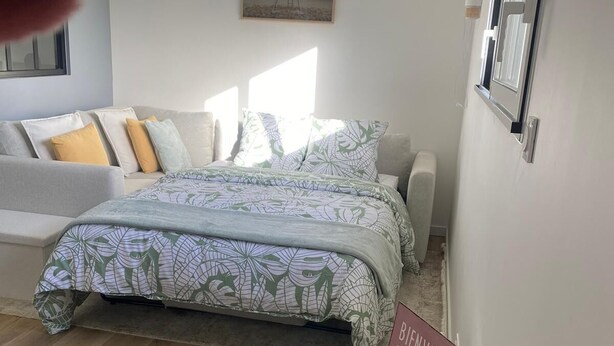 A bedroom with a bed, a bedside table with a water bottle, a coffee pot, and a sign that reads "Bienvenue".