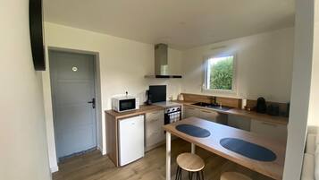 Een kleine keuken met een magnetron, fornuis, spoelbak en krukken.