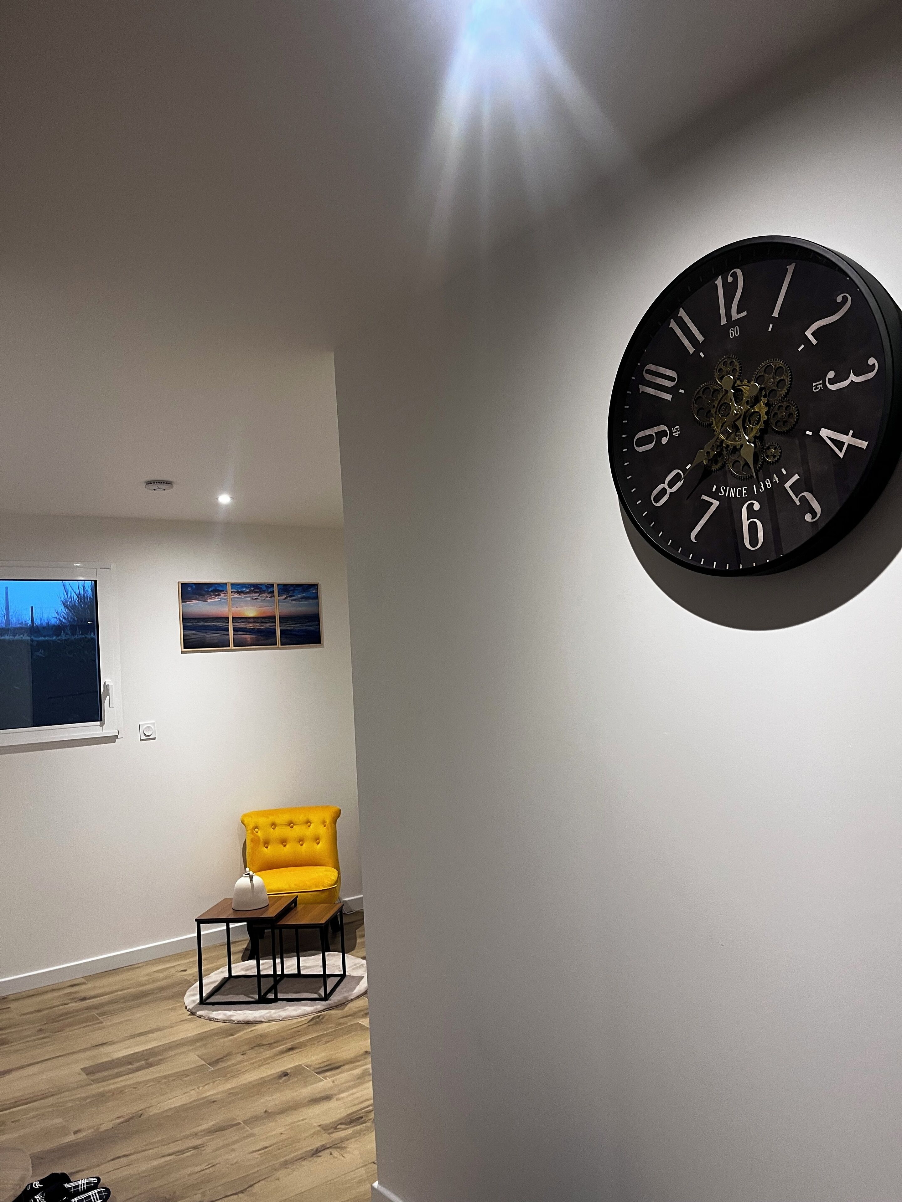 A modern living room with a large wall clock, a yellow armchair, and a wooden floor.