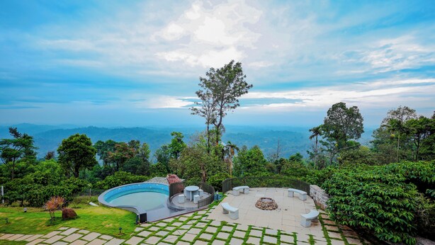 Uma área de piscina com vista para montanhas distantes, rodeada por vegetação exuberante e caminhos de pedra.