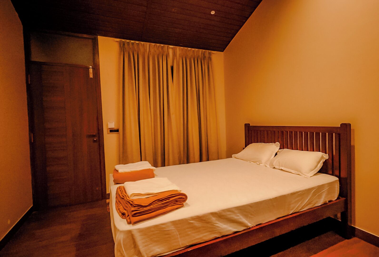 A single bed with a wooden headboard in a room with wooden flooring and a sloped ceiling.