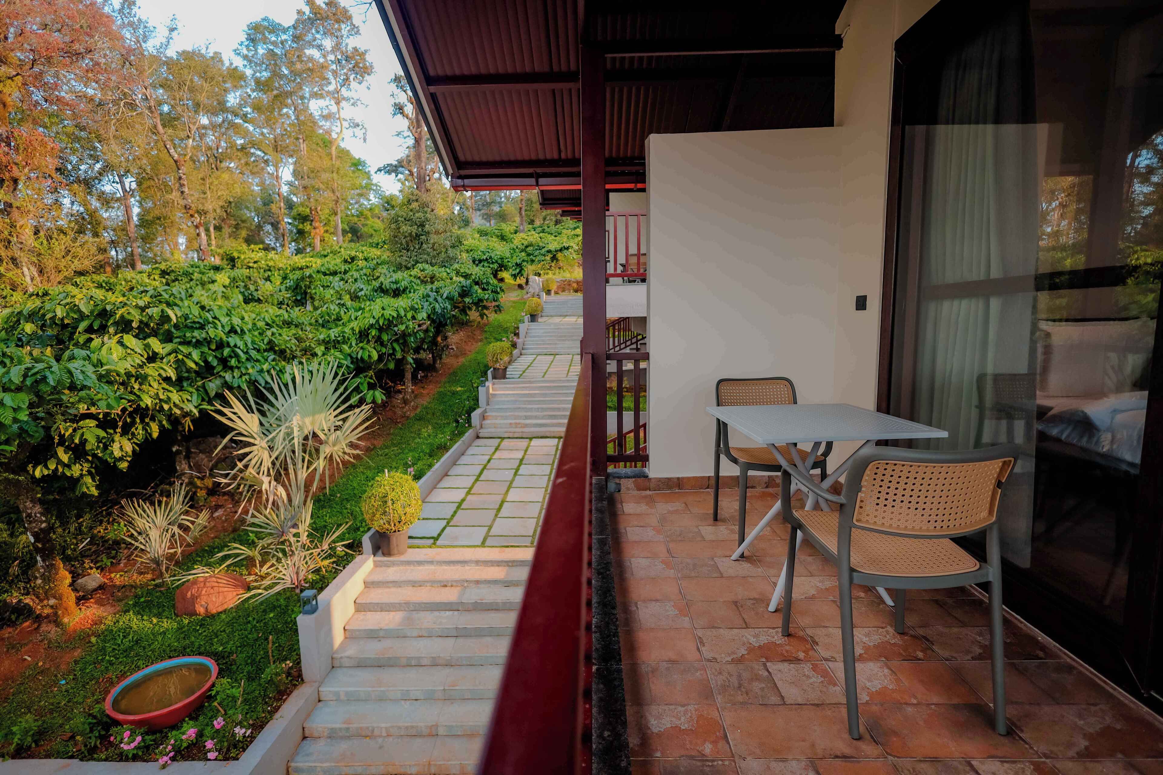 A patio with a table and chairs, a small garden with a pathway, and a view of the surrounding trees.