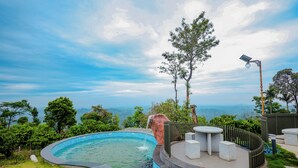 Piscina com vista para as montanhas, cercada por vegetação e um muro de madeira.
