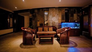 Uma sala de estar com sofá, duas poltronas, uma mesa de centro e um aquário.