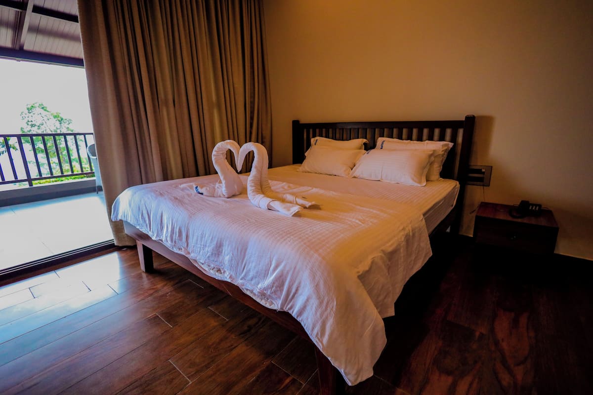 A hotel room with a large bed, wooden flooring, and a view of the outdoors through a window.