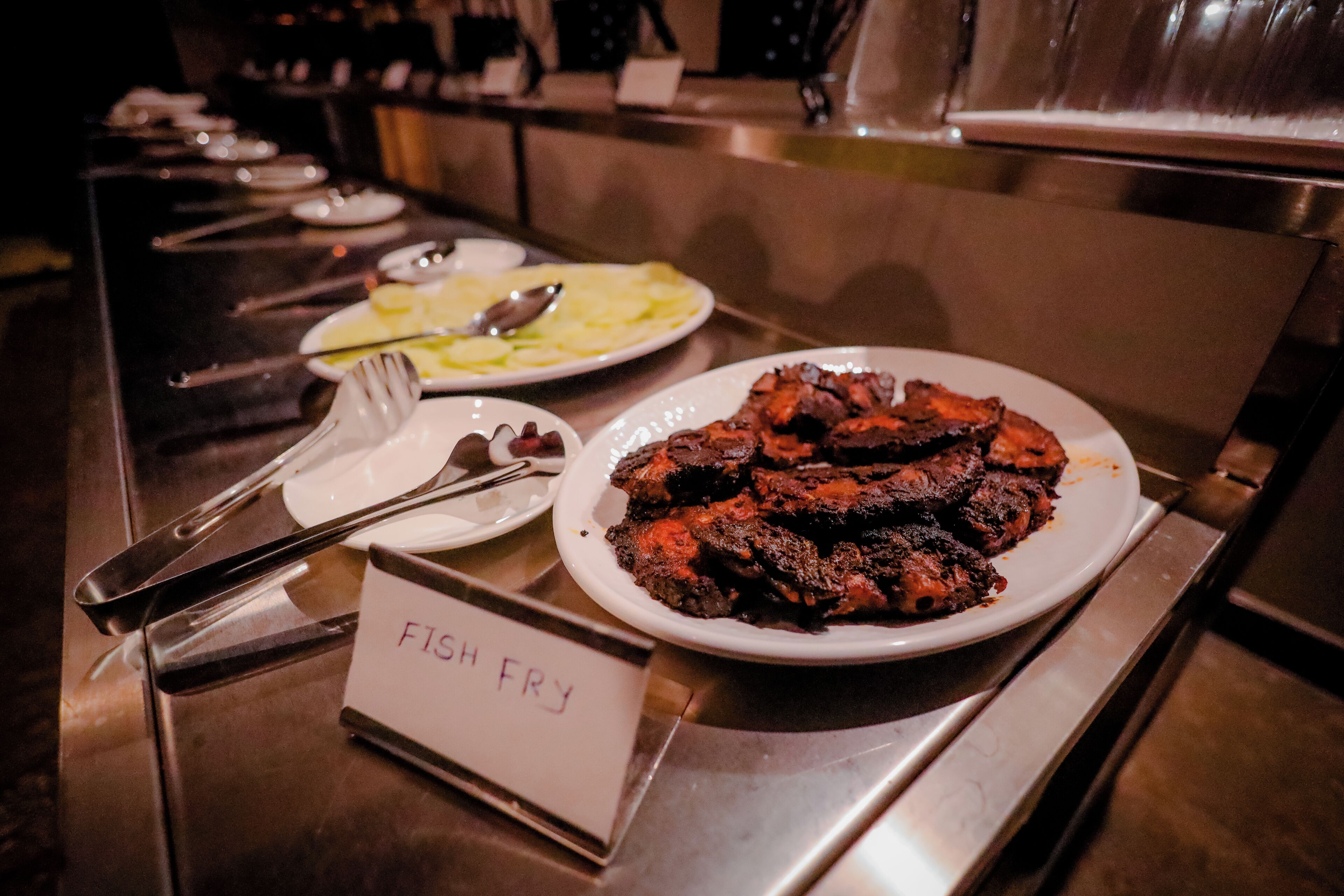 A buffet table with a sign labeled "FISH FRY" and plates of food, including fish and potatoes.