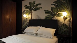 A neatly made bed with white linens, a wooden wardrobe, and wall-mounted lamps with a tropical mural. - Stay (Tsantsabane)