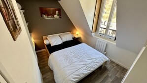 A bedroom with a bed, a nightstand, a lamp, a radiator, and a window with a view.