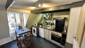 A compact kitchen with a washing machine, a dishwasher, a stove, and a TV mounted above the counter.