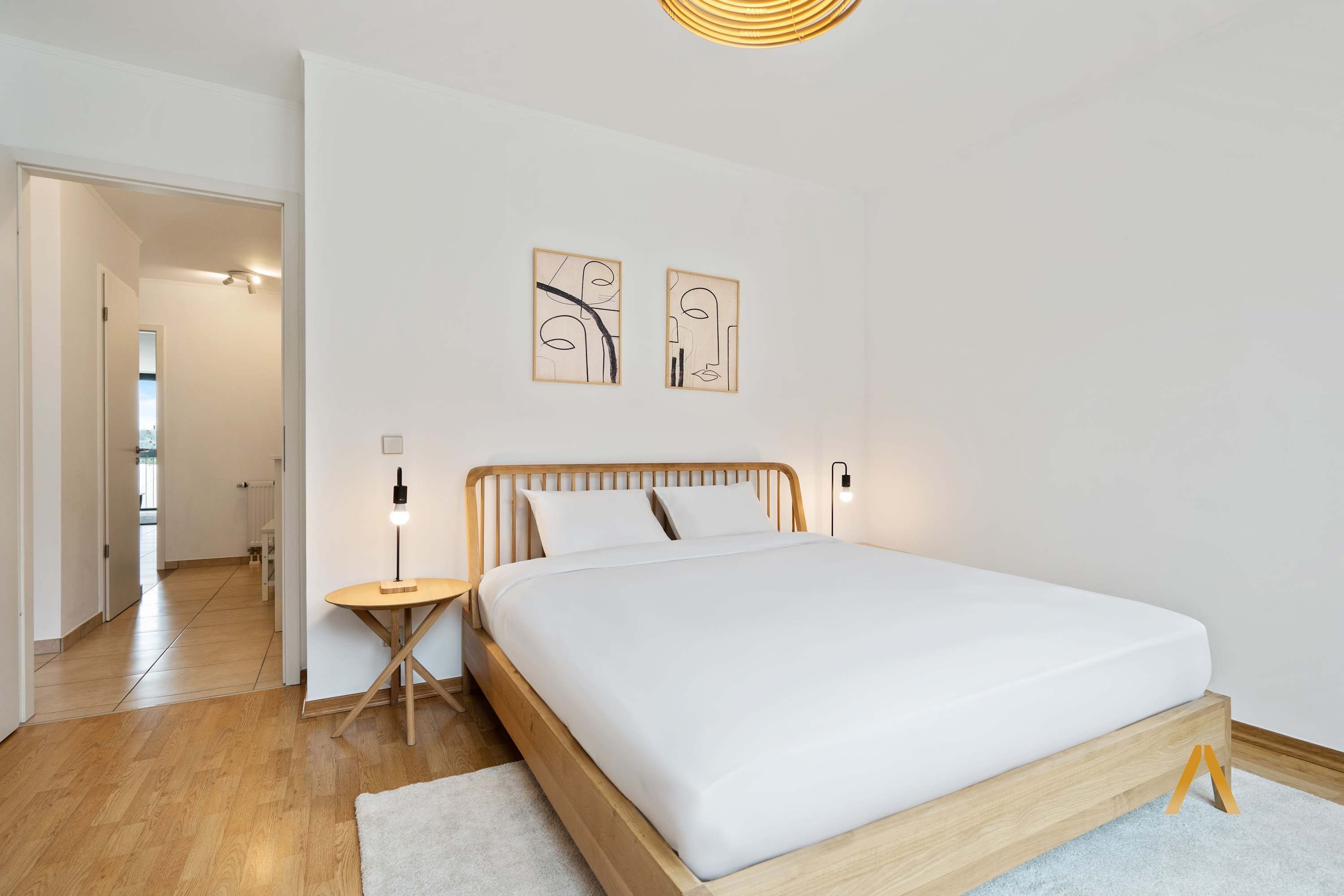 Un dormitorio con estructura de cama de madera, ropa de cama blanca y dos obras de arte abstractas en la pared.