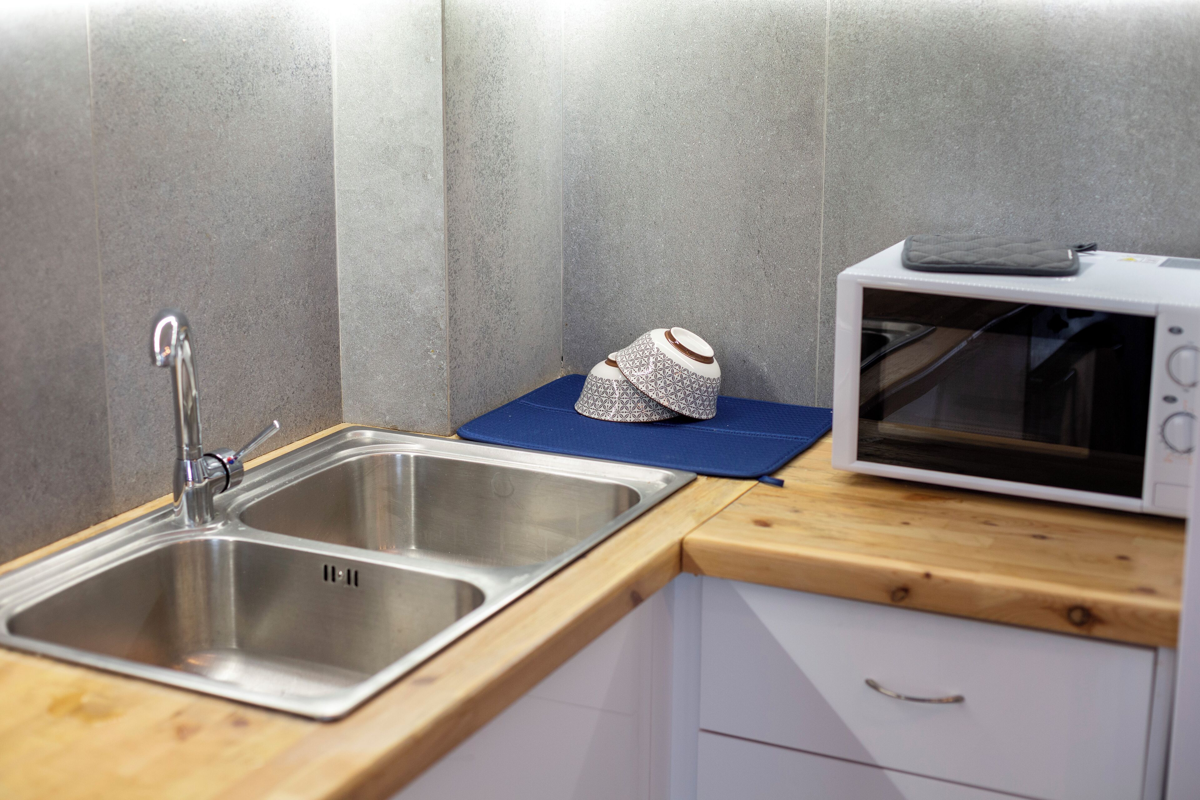 A kitchen with a stainless steel sink, a microwave, and a blue mat on the countertop.