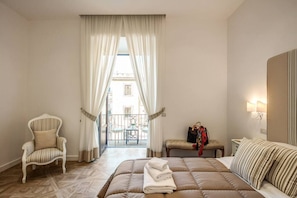 A hotel room with a bed, a chair, a bench, a table, and a view of the outside. - Sorrento Square Suites is an elegant guesthouse recently renovated, located in the center of Sorrento, right next to the renowned Piazza Tasso. Here you will find stylishly furnished rooms equipped with every comfort to ensure you a unique stay full of r (Sorrento)