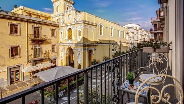 A balcony with outdoor seating, a yellow building with ornate architecture, and a clear sky. - Sorrento Square Suites is an elegant, newly renovated guesthouse located in the heart of Sorrento.Here, you'll find stylishly furnished rooms equipped with every comfort to ensure a unique stay focused on relaxation and convenience.You can also enjoy the (Sorrento)