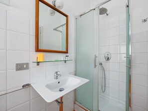 A bathroom with a white sink, a mirror with a wooden frame, a glass shower enclosure, and a glass shelf with toiletries.