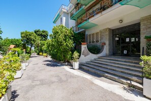 A building with a staircase leading to a gated entrance, surrounded by greenery and potted plants.