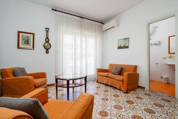 A living room with two orange sofas, a glass coffee table, and patterned flooring.
