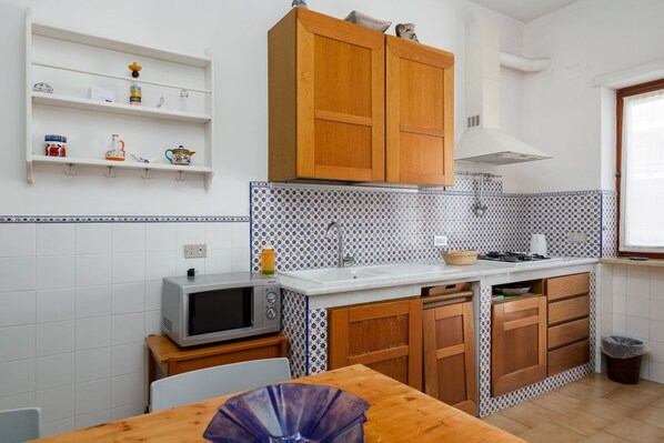 A compact kitchen with wooden cabinets, a microwave, and a tiled backsplash.