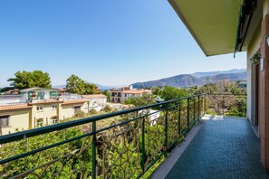A balcony with a view of a residential area, including houses and mountains in the distance.