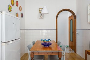 A compact kitchen with a white refrigerator, a wooden dining table with chairs, and a decorative bowl on the table.