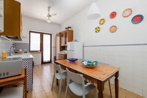 Uma cozinha com mesa de madeira, cadeiras, geladeira e micro-ondas.