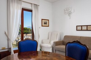 A room with a dining table, two chairs, a sofa, and a window with curtains.