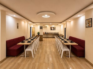 A conference room with a long table, white chairs, red sofas, and a ceiling light. - Hotel Royal Central Haridwar (Haridwar)
