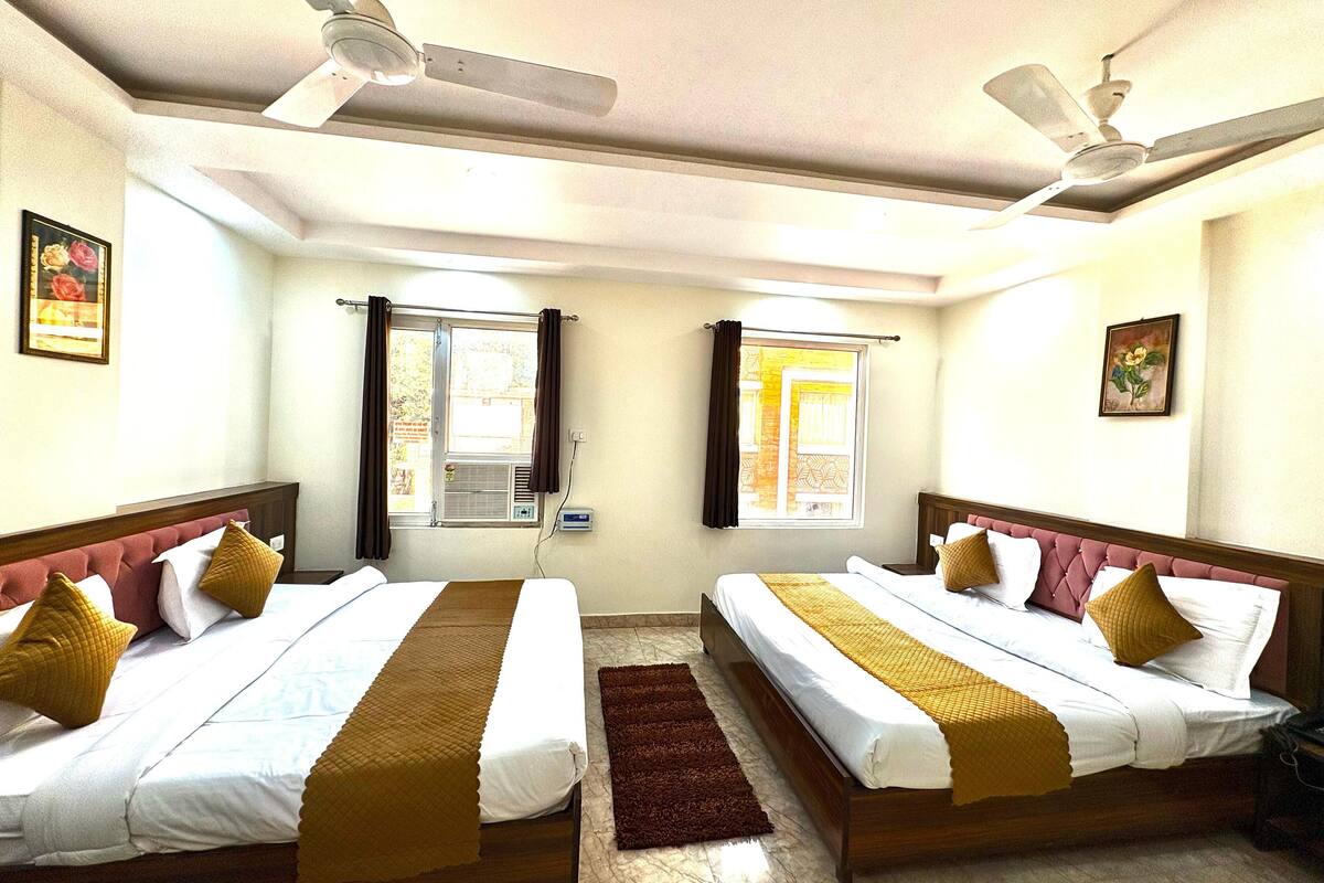 Habitación de hotel con dos camas, ventilador de techo, ventana con cortinas y una pequeña alfombra.