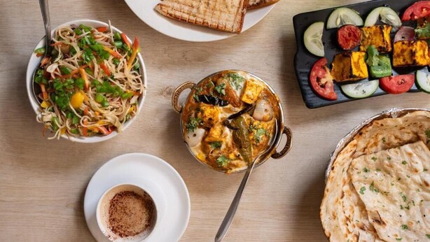 A variety of dishes including a salad, paneer tikka, and naan bread on a wooden table. - Hotel Royal Central Haridwar (Haridwar)
