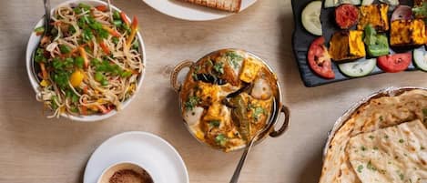 A variety of dishes including a salad, paneer tikka, and naan bread on a wooden table.